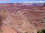 CANYONLANDS, <i>Shafer Trail Road</i>.<br>Ce chemin descend au fond d'un second canyon, devient <i>Potash Road</i> et finit par rejoindre le fleuve Colorado.<br>A l'horizon, les sommets enneigés des Montagnes Rocheuses.<br>Remarquez la taille du véhicule sur la piste, en bas et au centre de l'image: c'est vraiment géant !